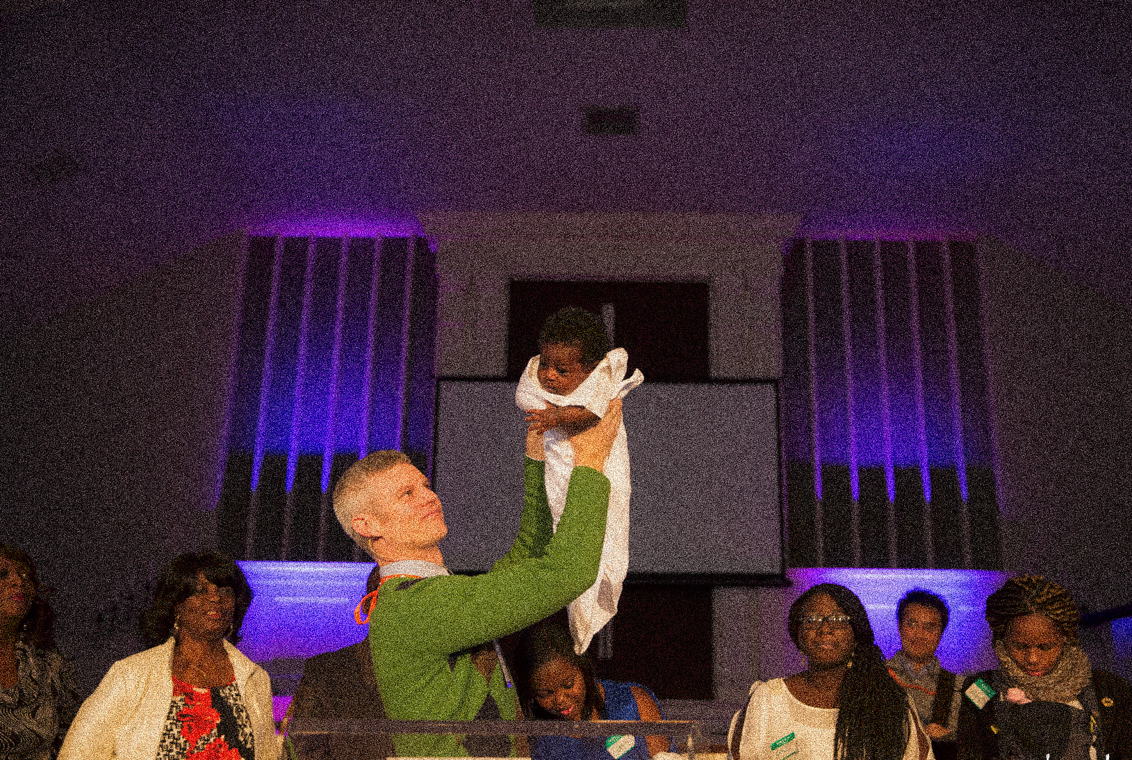 Pastor Stephen lifting a baby up to present to the church after it's dedication